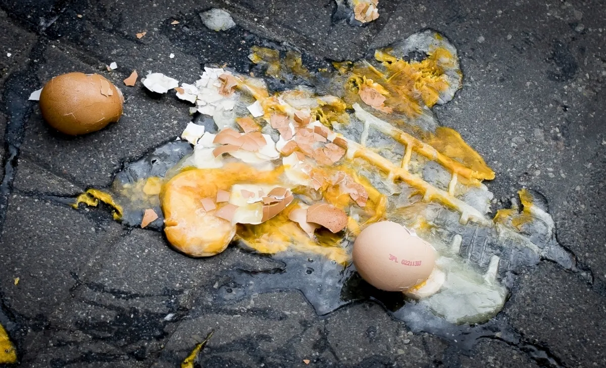 Broken eggs spilled across dark pavement with yolk and crushed shells